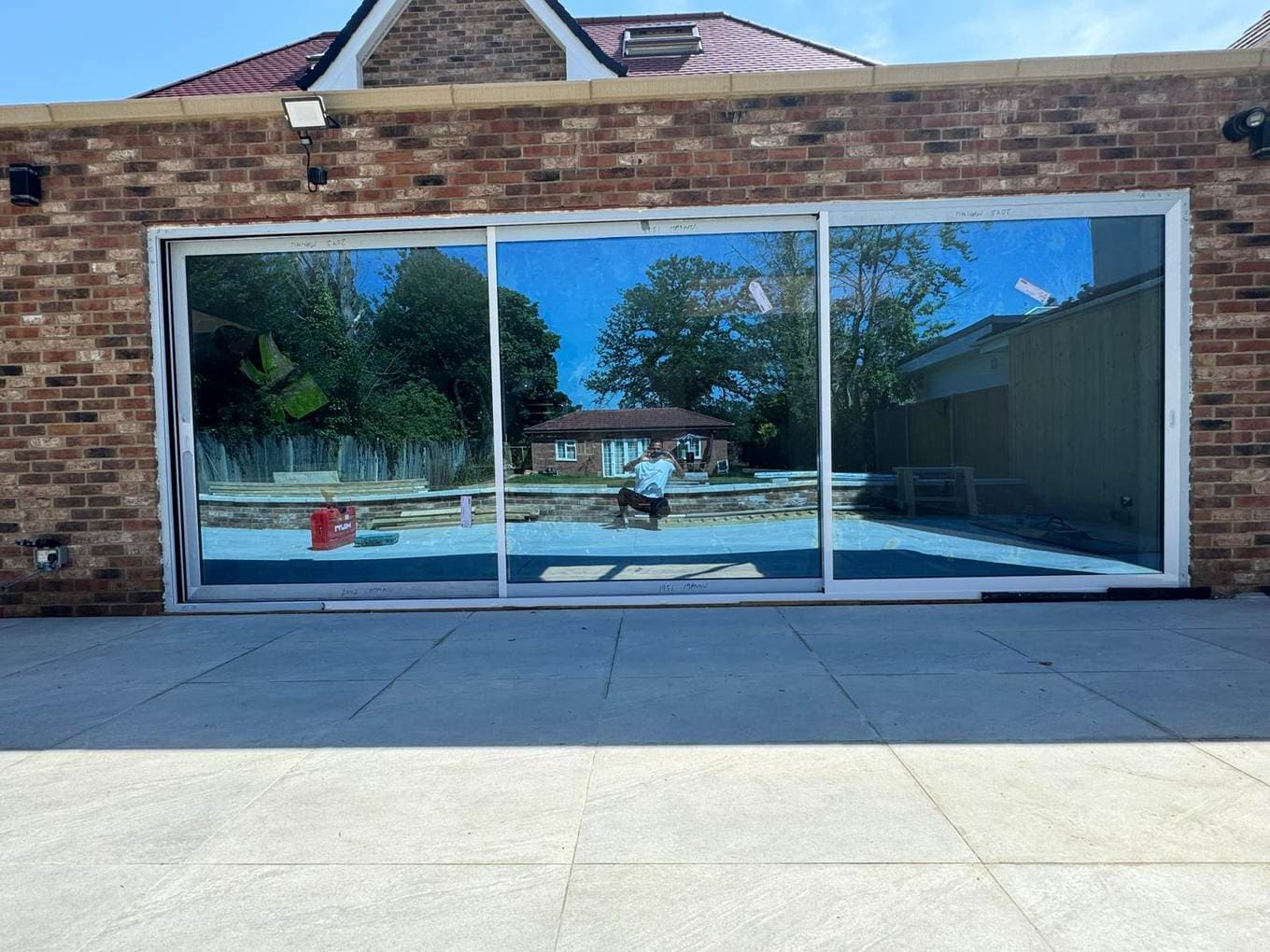 Three-panel aluminium sliding door reflecting a garden and pool
